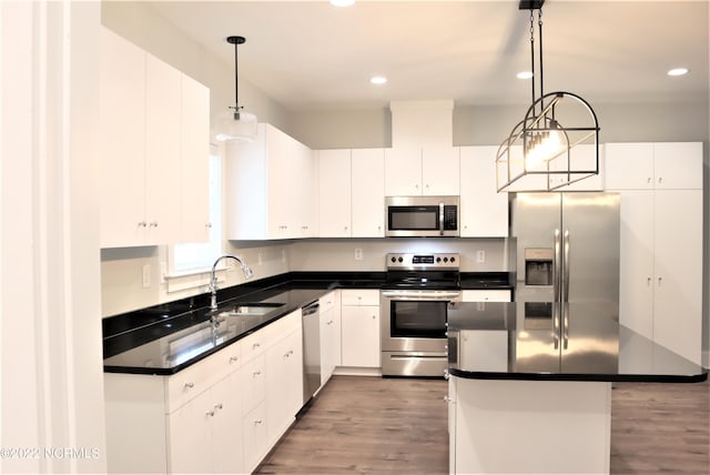 kitchen with dark countertops, appliances with stainless steel finishes, white cabinetry, a sink, and wood finished floors