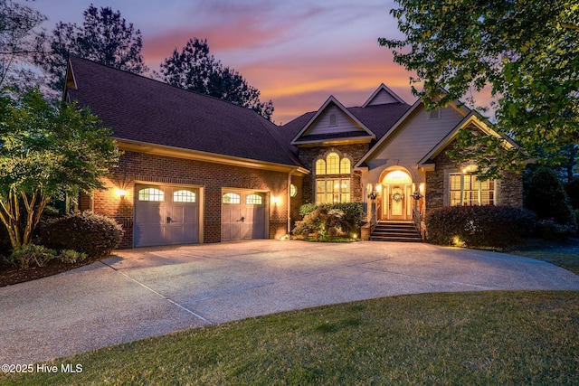 view of front of house featuring an attached garage, a shingled roof, brick siding, and driveway