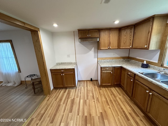 kitchen featuring light stone countertops, light wood-type flooring, and sink