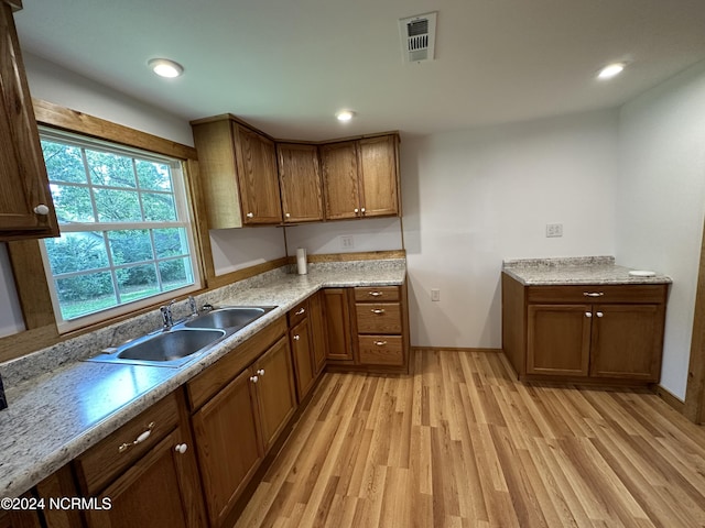 kitchen with light stone countertops, light hardwood / wood-style flooring, and sink