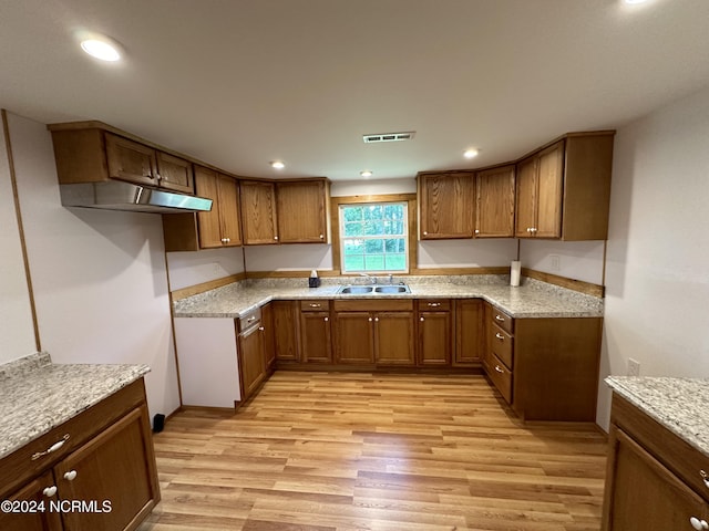 kitchen featuring light wood-type flooring, light stone counters, and sink