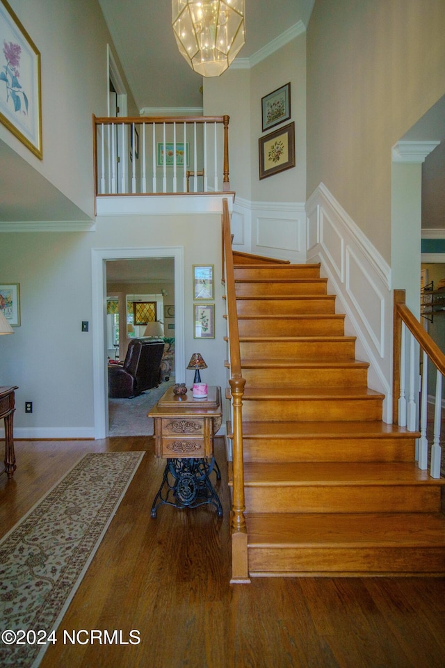 staircase with hardwood / wood-style floors, crown molding, a notable chandelier, and a high ceiling