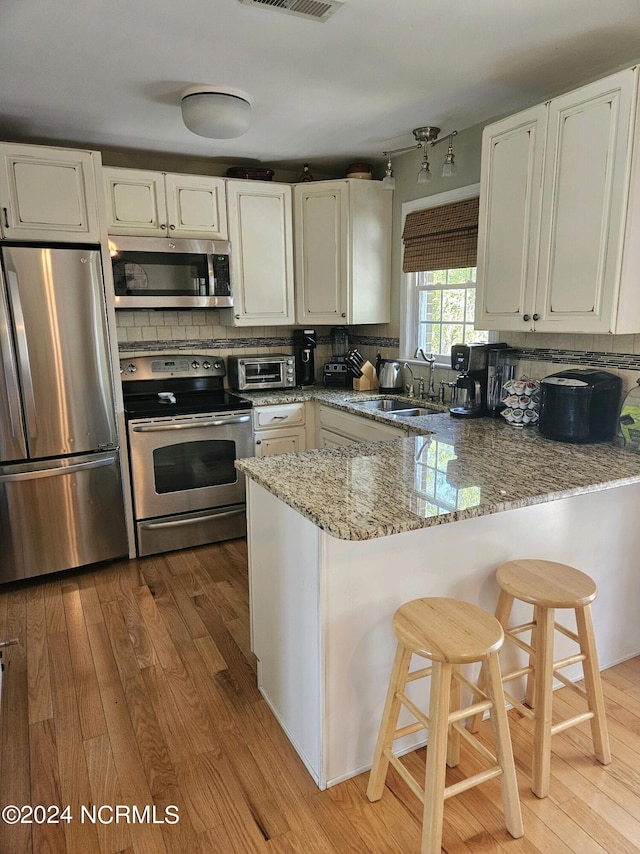 kitchen with light stone counters, a peninsula, stainless steel appliances, white cabinetry, and a sink