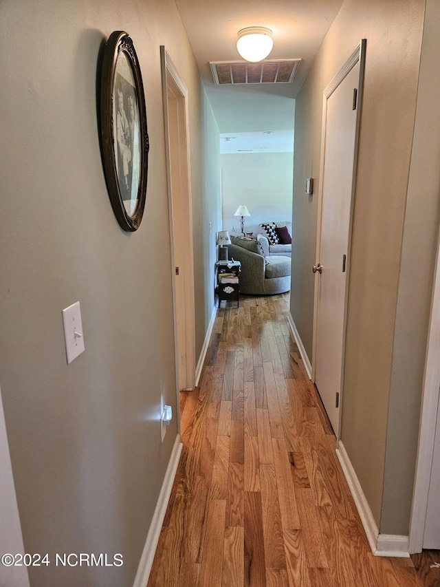 hallway with light wood-style flooring, visible vents, and baseboards