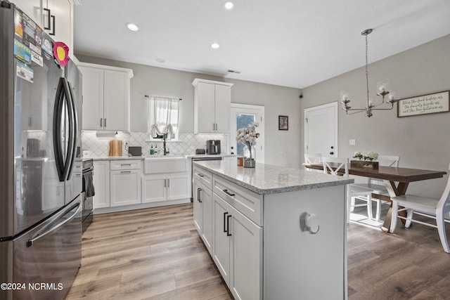 kitchen with backsplash, light wood-style floors, freestanding refrigerator, and a sink