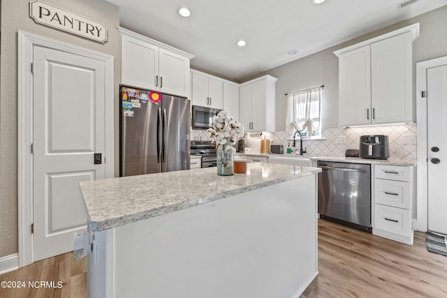 kitchen featuring light wood-type flooring, stainless steel appliances, a kitchen island, and white cabinetry