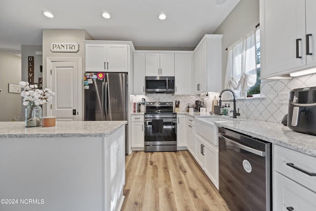 kitchen with light wood finished floors, appliances with stainless steel finishes, white cabinetry, and a sink