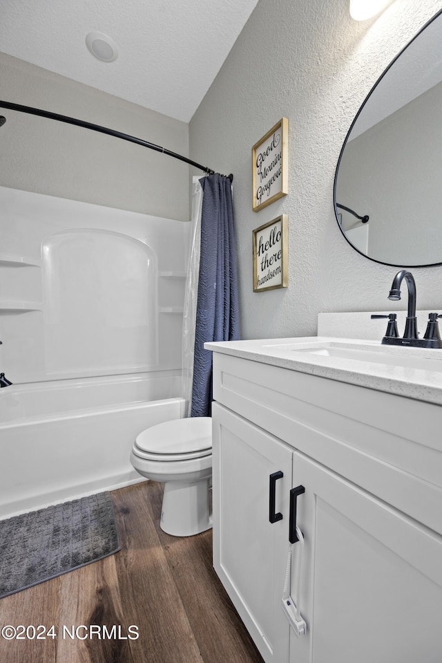 bathroom with toilet, shower / bath combo with shower curtain, wood finished floors, a textured wall, and vanity