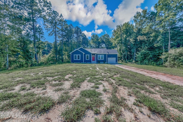 single story home featuring a front yard, a forest view, a garage, and driveway