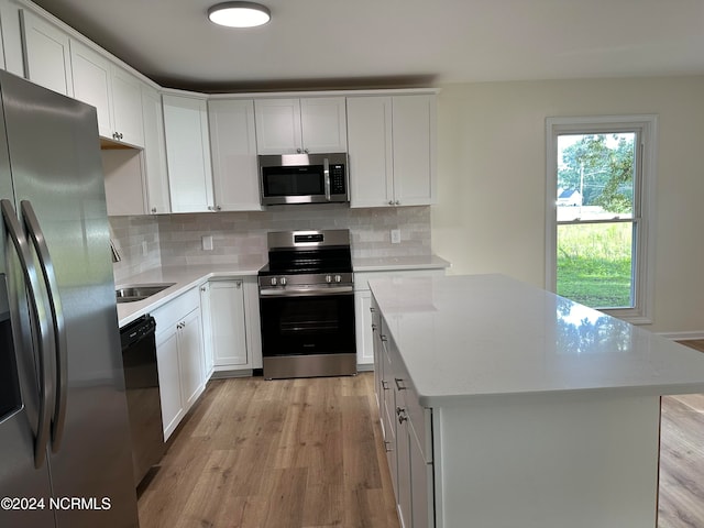 kitchen with white cabinets, appliances with stainless steel finishes, a kitchen island, and light hardwood / wood-style flooring