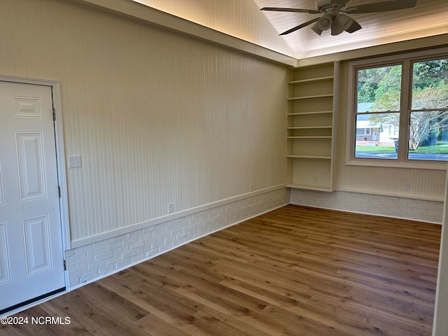 empty room featuring lofted ceiling, wood-type flooring, ceiling fan, and wooden walls