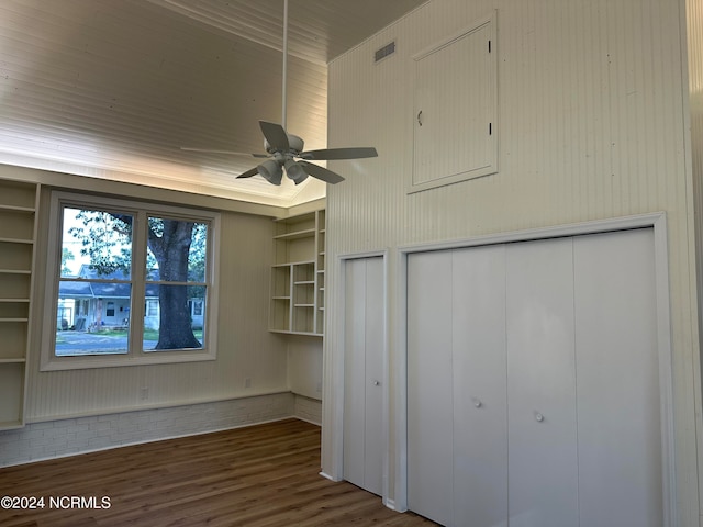 unfurnished living room featuring built in features, ceiling fan, wooden walls, and dark hardwood / wood-style flooring