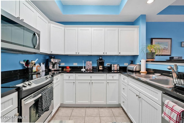 kitchen with white cabinetry, appliances with stainless steel finishes, light tile patterned floors, and a raised ceiling