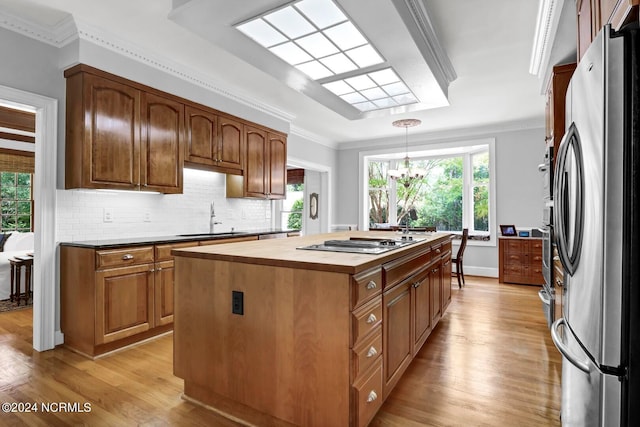 kitchen featuring light wood-type flooring, appliances with stainless steel finishes, a center island with sink, tasteful backsplash, and ornamental molding