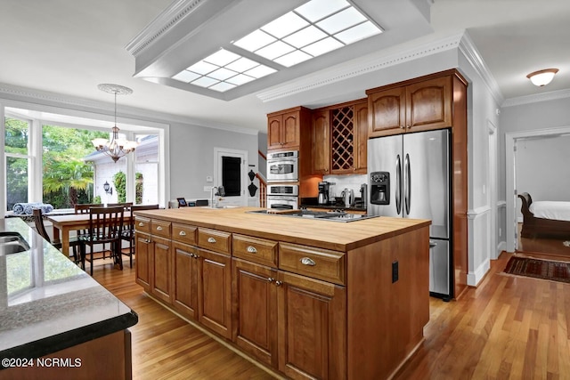 kitchen with appliances with stainless steel finishes, a kitchen island, butcher block counters, and ornamental molding