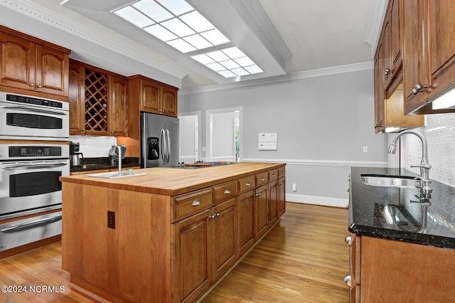 kitchen featuring backsplash, light wood-type flooring, appliances with stainless steel finishes, an island with sink, and butcher block counters