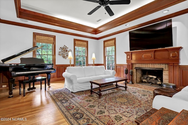 living room featuring plenty of natural light, light hardwood / wood-style flooring, a brick fireplace, and a raised ceiling