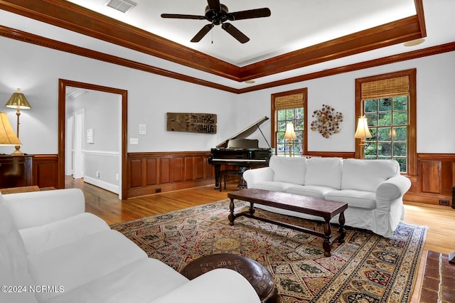 living room with crown molding, wood-type flooring, a tray ceiling, and ceiling fan