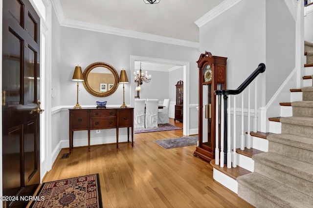 foyer entrance featuring light wood-type flooring, a notable chandelier, and ornamental molding