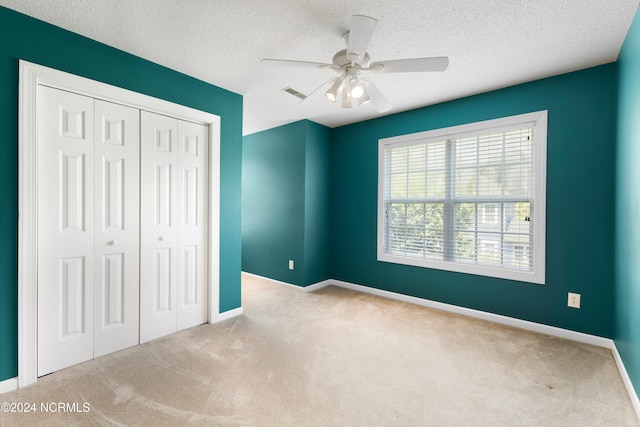 unfurnished bedroom with ceiling fan, a closet, a textured ceiling, and light carpet