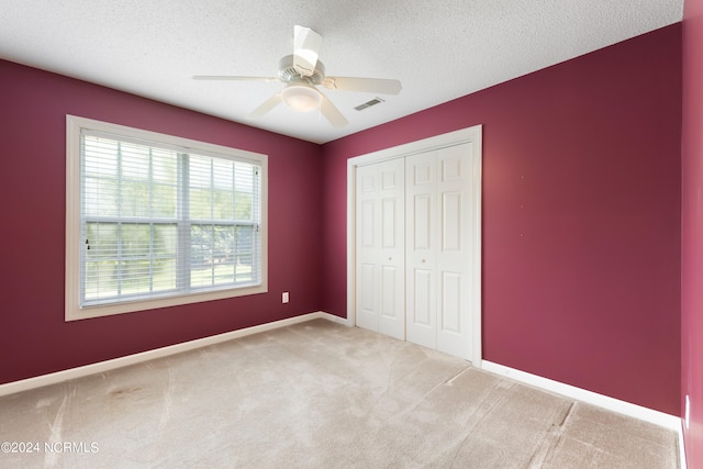 unfurnished bedroom with ceiling fan, a closet, a textured ceiling, and light colored carpet