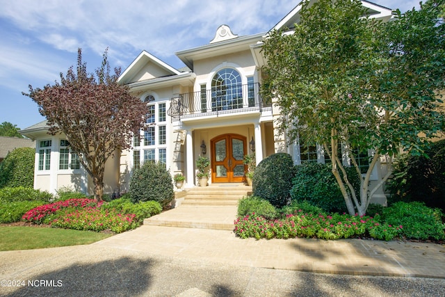 view of front facade with a balcony, stucco siding, and french doors