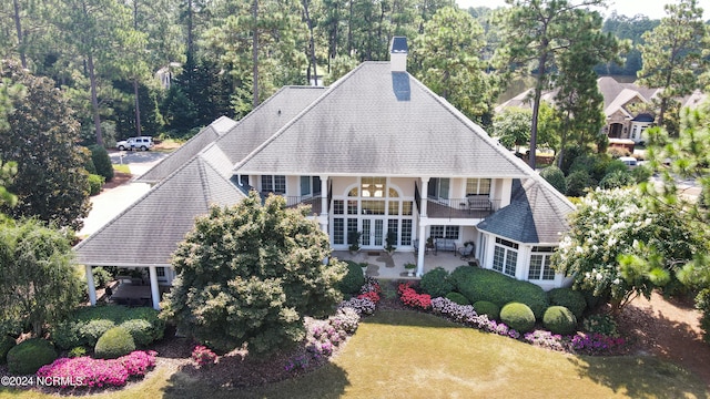 exterior space with a chimney, a patio, a balcony, and a front lawn