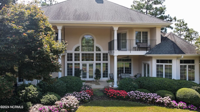 rear view of house with french doors, roof with shingles, a balcony, and stucco siding