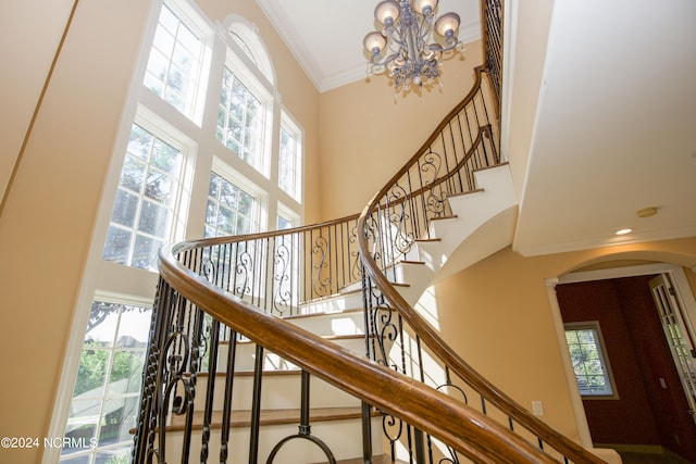 staircase with a towering ceiling, plenty of natural light, arched walkways, and crown molding