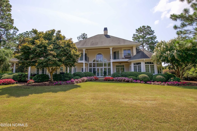 greek revival inspired property featuring a chimney, a balcony, a front lawn, and stucco siding