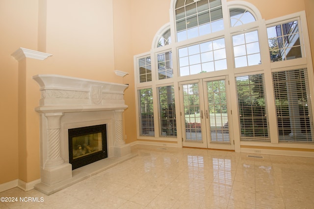 unfurnished living room featuring plenty of natural light, a high ceiling, baseboards, and a glass covered fireplace