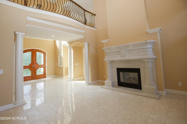 unfurnished living room with a high ceiling, baseboards, french doors, a glass covered fireplace, and decorative columns