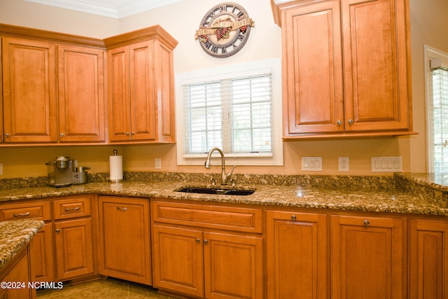 kitchen featuring dark stone counters, brown cabinetry, a sink, and crown molding