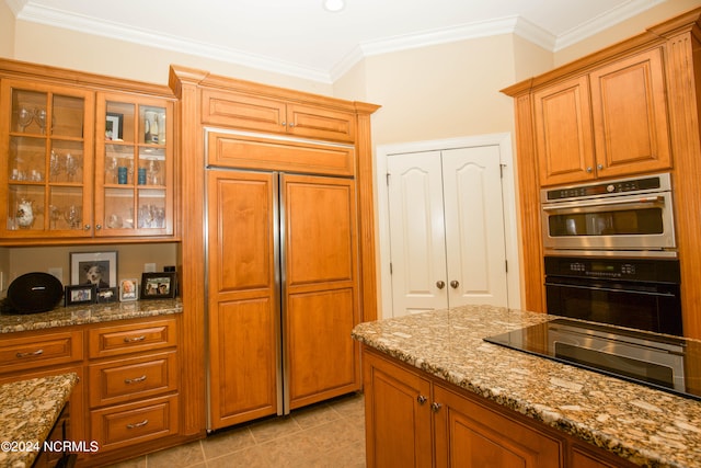 kitchen with paneled fridge, light stone counters, stainless steel double oven, glass insert cabinets, and crown molding