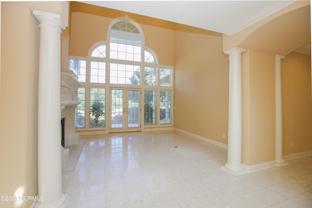 unfurnished living room with a fireplace with raised hearth, a healthy amount of sunlight, baseboards, and ornate columns