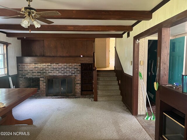 carpeted living room with ceiling fan, beam ceiling, and a brick fireplace