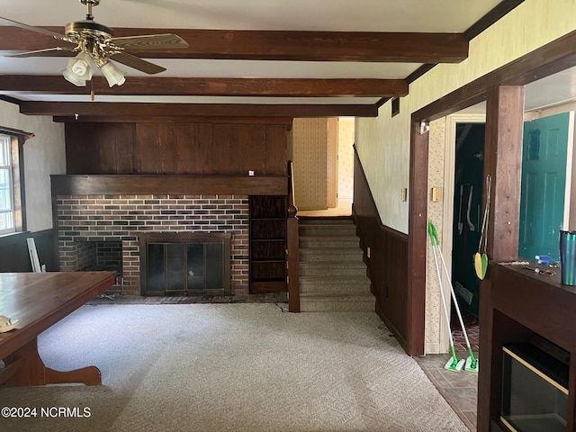 living room featuring stairs, a brick fireplace, beam ceiling, and wooden walls