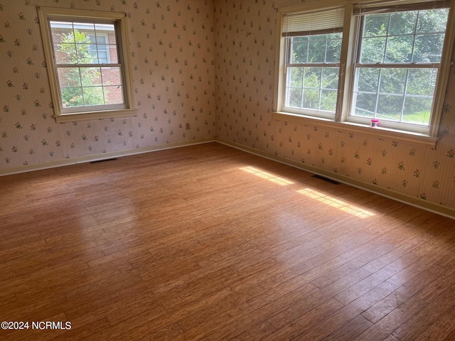 unfurnished room featuring light wood-type flooring, visible vents, baseboards, and wallpapered walls