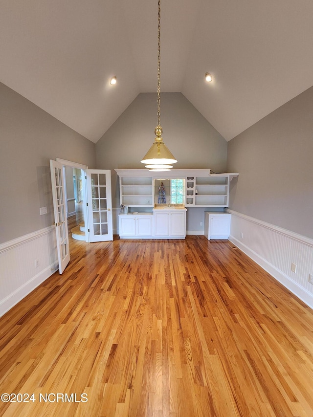 unfurnished living room featuring wainscoting, french doors, light wood-type flooring, and lofted ceiling