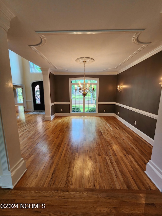 empty room with decorative columns, crown molding, an inviting chandelier, and wood finished floors