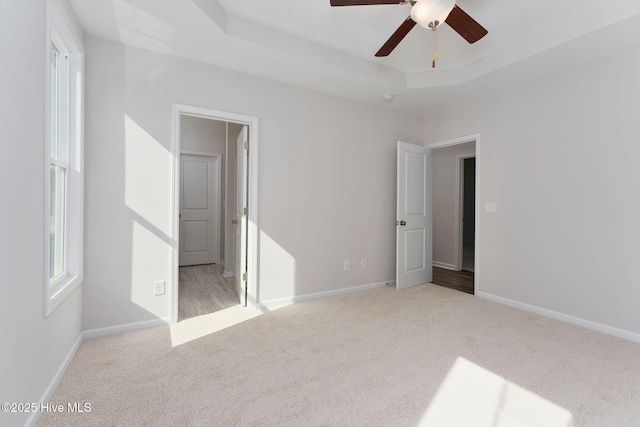 unfurnished bedroom with a tray ceiling, light colored carpet, and ceiling fan