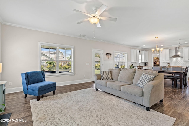 living room featuring dark hardwood / wood-style floors, ornamental molding, ceiling fan with notable chandelier, and a healthy amount of sunlight