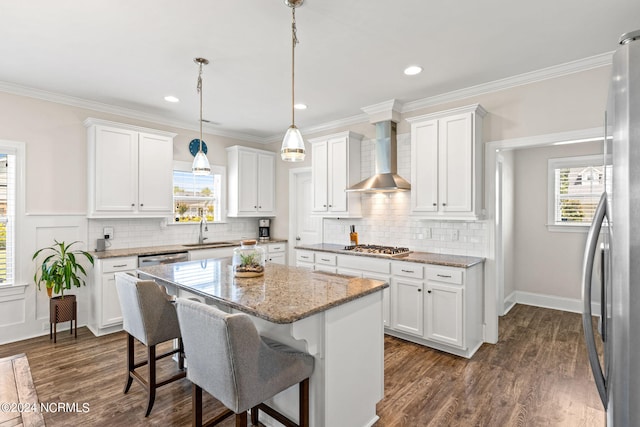 kitchen with wall chimney range hood, white cabinets, sink, and a kitchen island