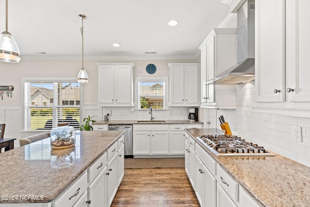 kitchen featuring wall chimney range hood, hanging light fixtures, appliances with stainless steel finishes, white cabinetry, and wood-type flooring