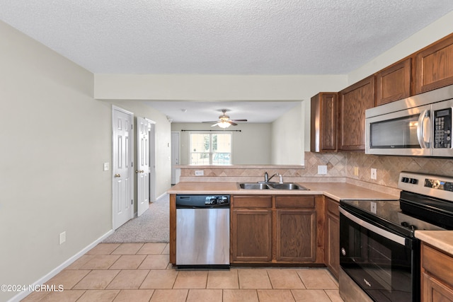 kitchen with appliances with stainless steel finishes, kitchen peninsula, sink, decorative backsplash, and ceiling fan