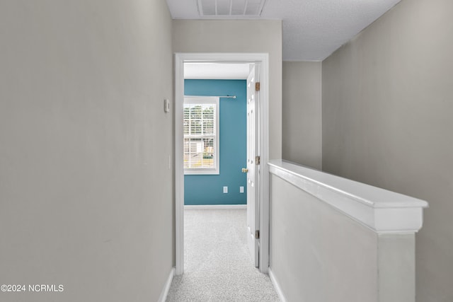 hall featuring light colored carpet and a textured ceiling