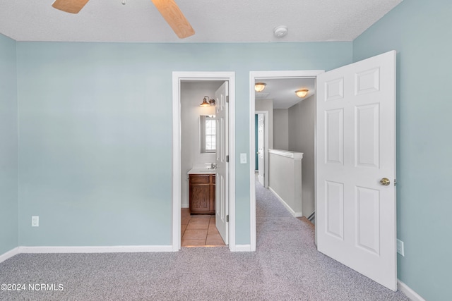 unfurnished bedroom featuring ceiling fan, a textured ceiling, light carpet, and ensuite bath