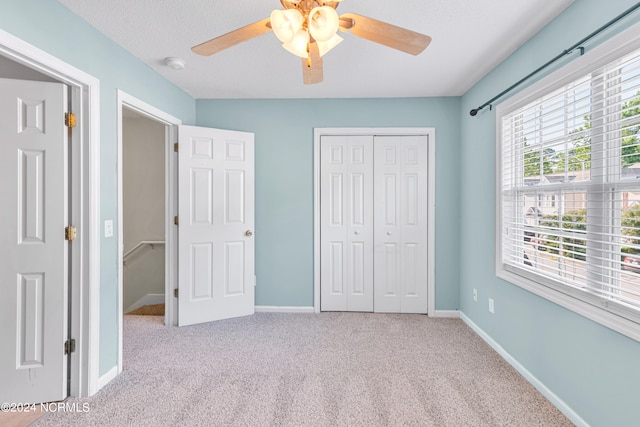 unfurnished bedroom with light carpet, a textured ceiling, ceiling fan, and a closet