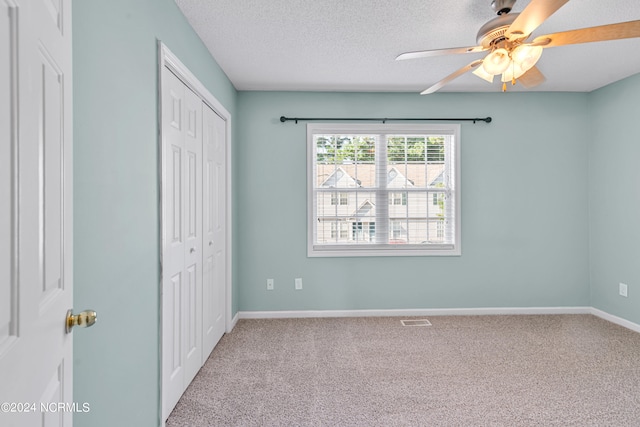 unfurnished bedroom with a closet, a textured ceiling, ceiling fan, and carpet floors