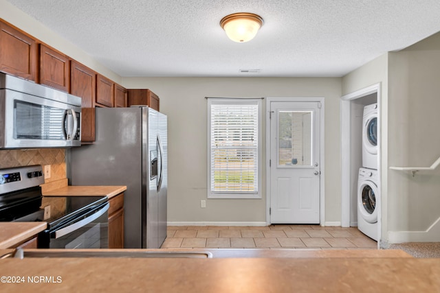 kitchen featuring light tile patterned floors, a textured ceiling, stacked washer and clothes dryer, and stainless steel appliances